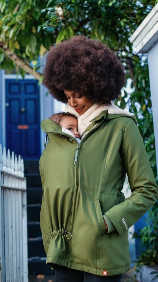 Mujer porteando a su bebé delante con el abrigo Wallaby en un parque otoñal